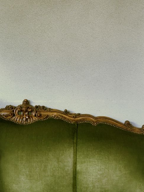 A close-up of an antique-style sofa with a green velvet upholstery and an ornate wooden frame with intricate carvings, situated against a plain, light-colored wall. The sofa appears clean and well-maintained, showcasing smooth fabric without visible dust or stains. The lighting is soft, illuminating the detailed woodwork and the rich texture of the velvet. This image exemplifies surface cleaning and maintenance suitable for period homes, as offered by Fulham Carpet Cleaning. The setting suggests a cozy, traditional interior space focused on aesthetic preservation through professional cleaning services.
